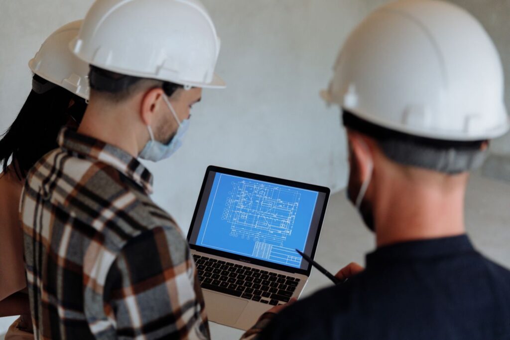 Site team in hard hats reviewing a project plan on a laptop